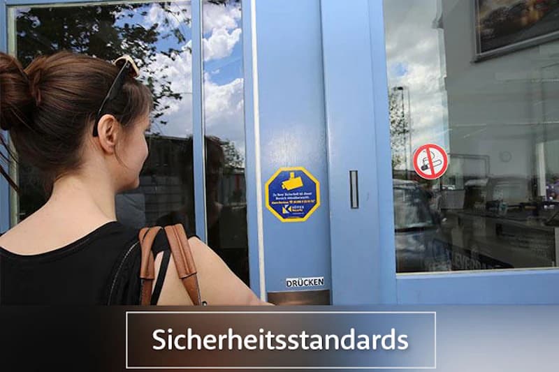Frau von hinten mit Tasche vor blauer Glastür mit Aufklebern und Drücken-Schild.