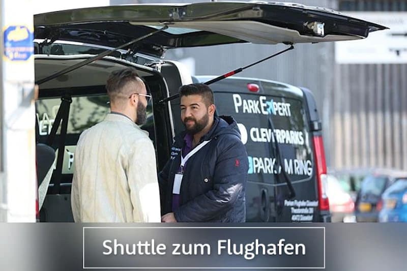 Zwei Männer stehen am geöffneten Heck eines Shuttle-Vans mit Firmenbeschriftung.