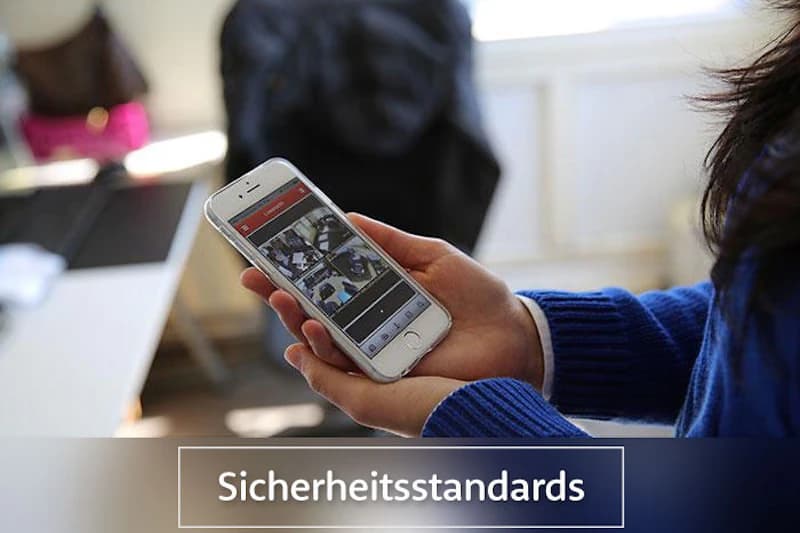 Hand hält Smartphone mit vier Überwachungsbildern auf dem Display und dem Schriftzug Sicherheitsstandards.