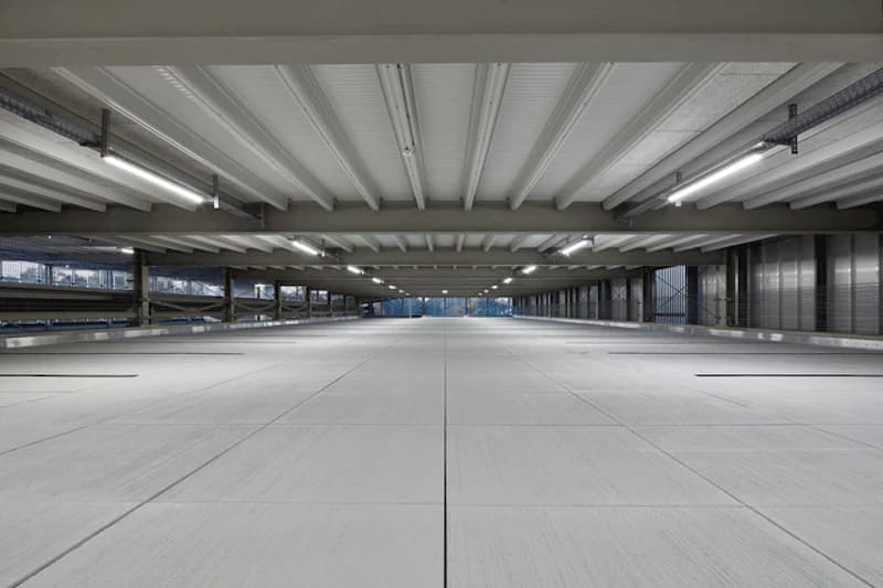 Leeres überdachtes Parkdeck mit Betonboden, Deckenleuchten und seitlichen Gittergeländern.