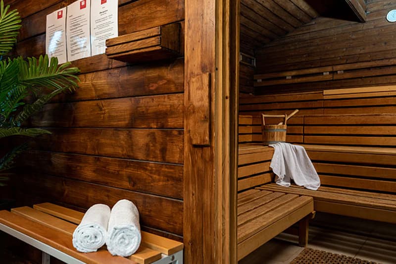 Holzsauna mit Sitzbänken, Holzeimer und zwei zusammengerollten Handtüchern auf einer Ablage.