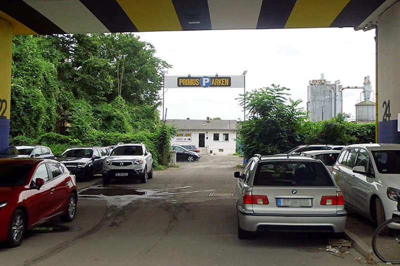 Überdachte Zufahrt zu Parkplatz mit geparkten Autos und Schild Primus Parken über der Einfahrt.