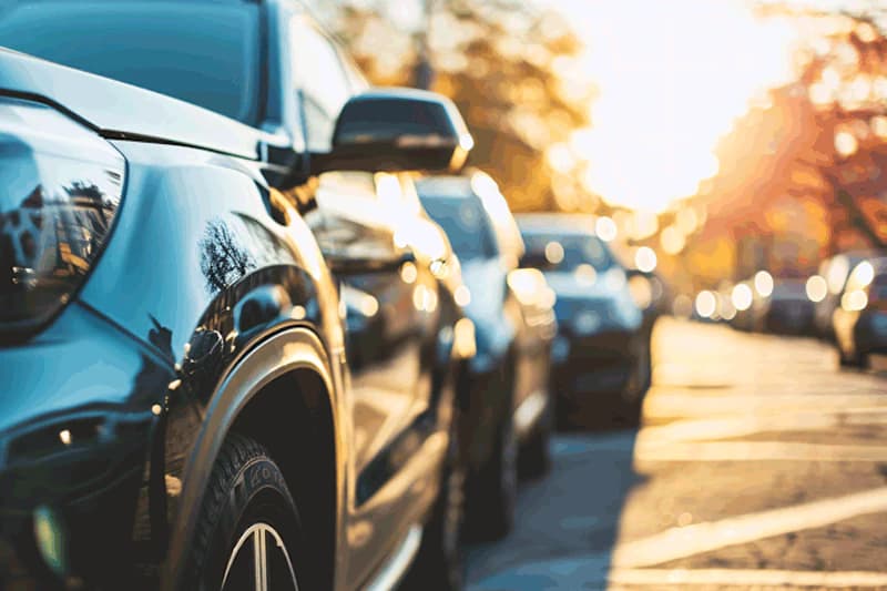 Reihe geparkter Autos in Abendsonne, Nahaufnahme des vorderen Fahrzeugs.