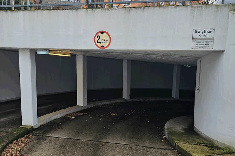 Geschwungene Zufahrt in eine Tiefgarage mit Durchfahrthöhenzeichen 2,05 m und weißen Stützen.