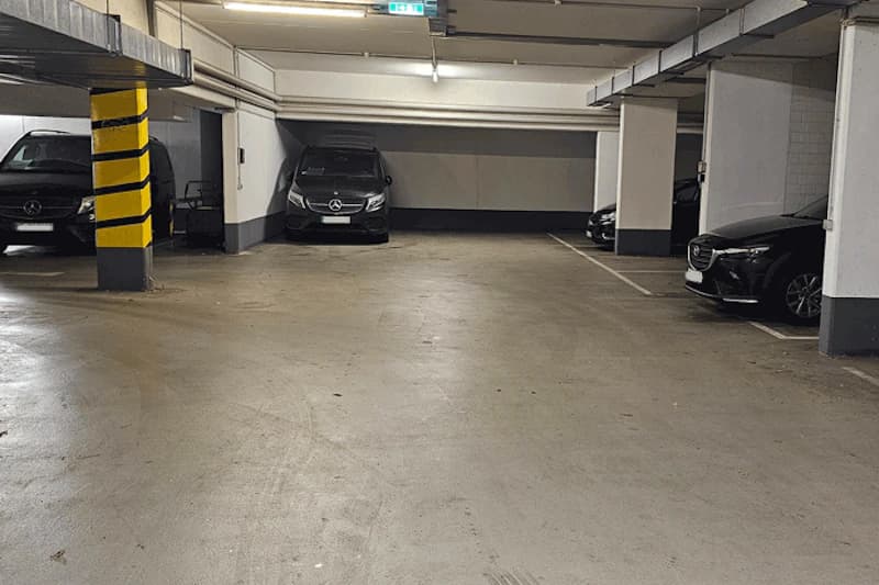 Unterirdische Parkebene mit mehreren geparkten schwarzen Autos und markiertem Stützpfeiler mit schwarz-gelben Streifen.