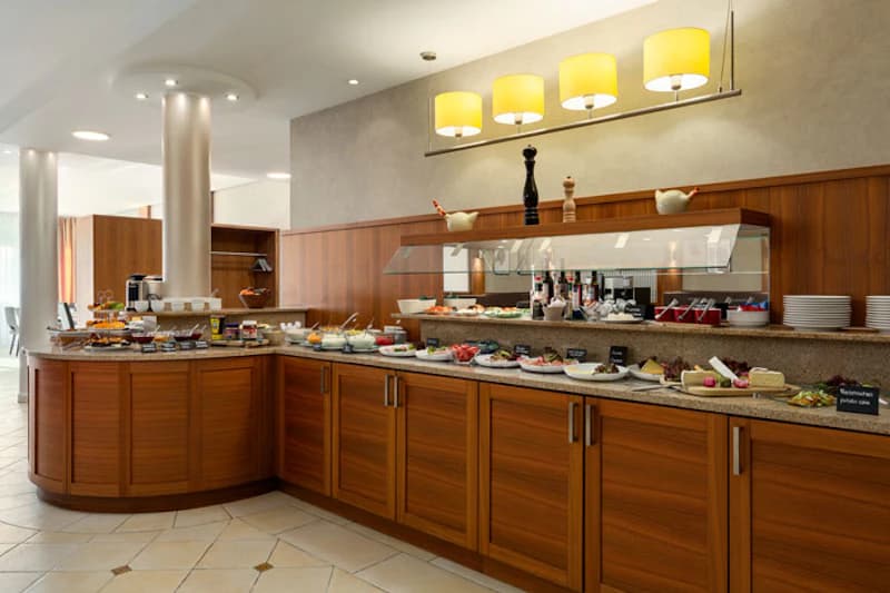 Buffet mit Holztheke, Schalen mit Speisen, Tellern und drei gelben Hängeleuchten über der Theke.