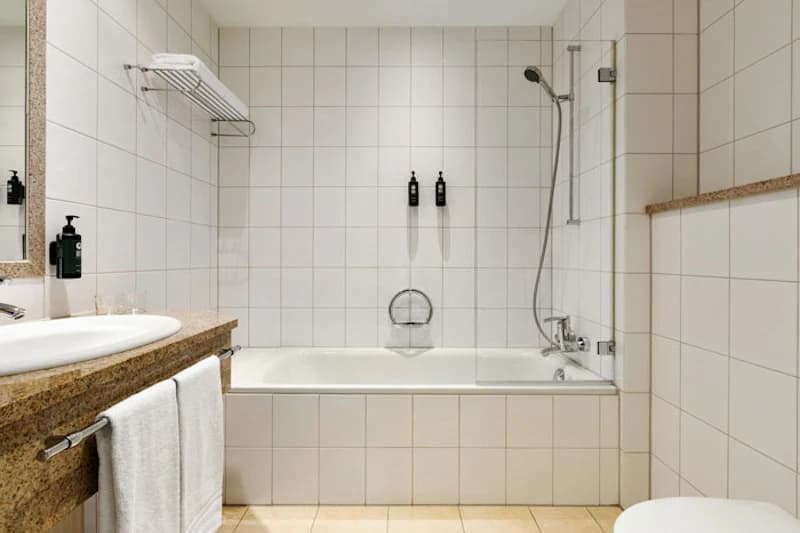 Weisses Badezimmer mit Badewanne, Duschkopf, Waschbecken, Handtuch und weißen Wandfliesen.