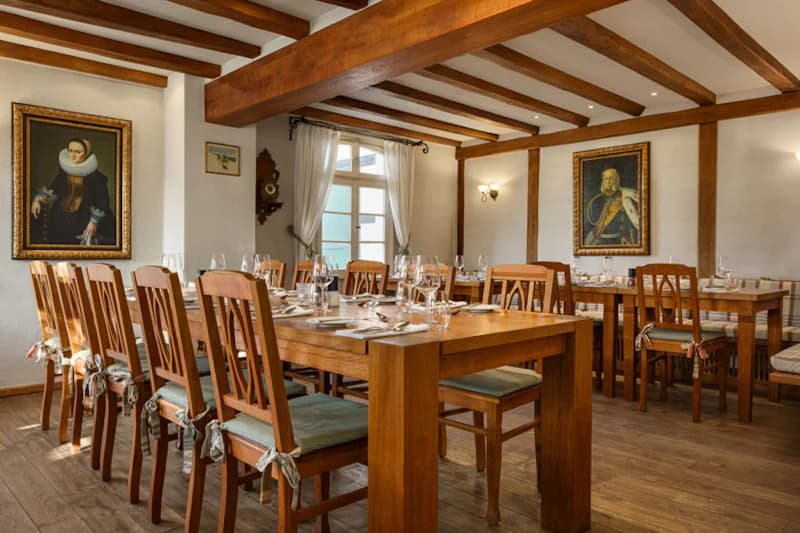 Heller Speisesaal mit Holztischen und eingedeckten Plätzen, sichtbaren Deckenbalken und Wandporträts.