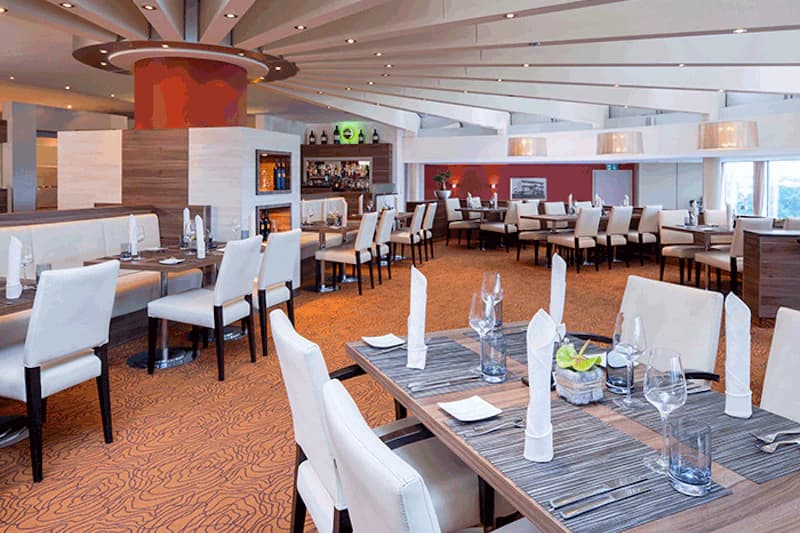 Hotelrestaurant mit eingedeckten Tischen, weißen Stühlen, rotem Säulenelement und Bar im Hintergrund.