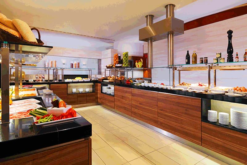Buffet mit Theken, frischem Obst, Backwaren und Tellern in einem gut beleuchteten Speisesaal.