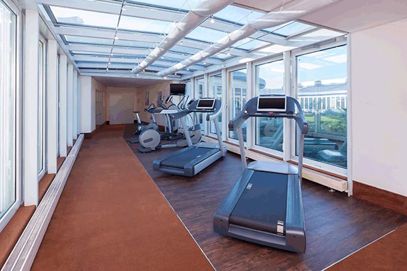 Fitnessraum mit Laufbändern, Crosstrainern, großflächigen Fenstern und Glasdach.