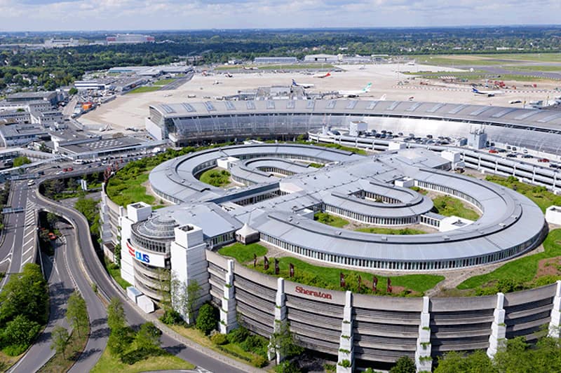 Luftaufnahme eines runden Parkhauses mit Sheraton-Schriftzug, Flughafen-Terminal und Rollfeld im Hintergrund.