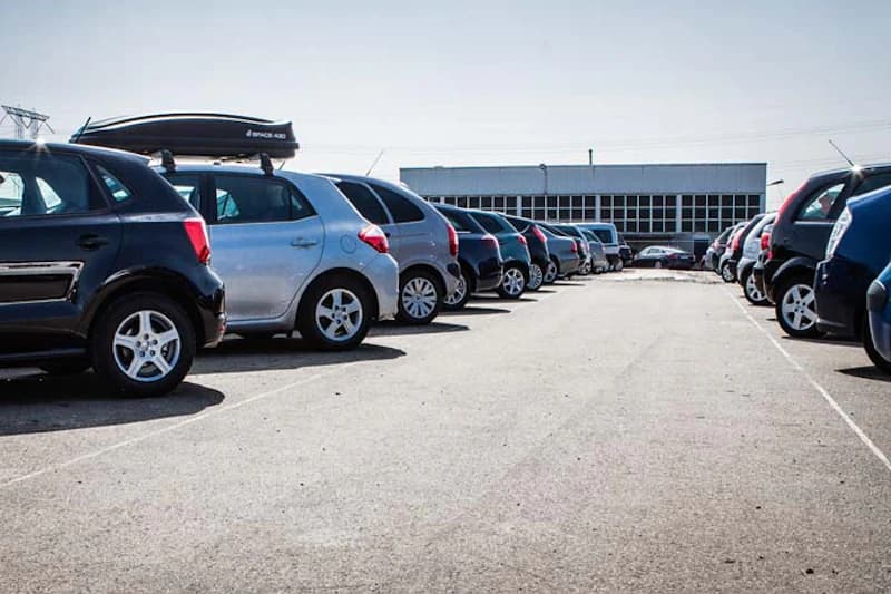 Reihen geparkter Autos auf Außenparkplatz vor niedrigem Gebäude.