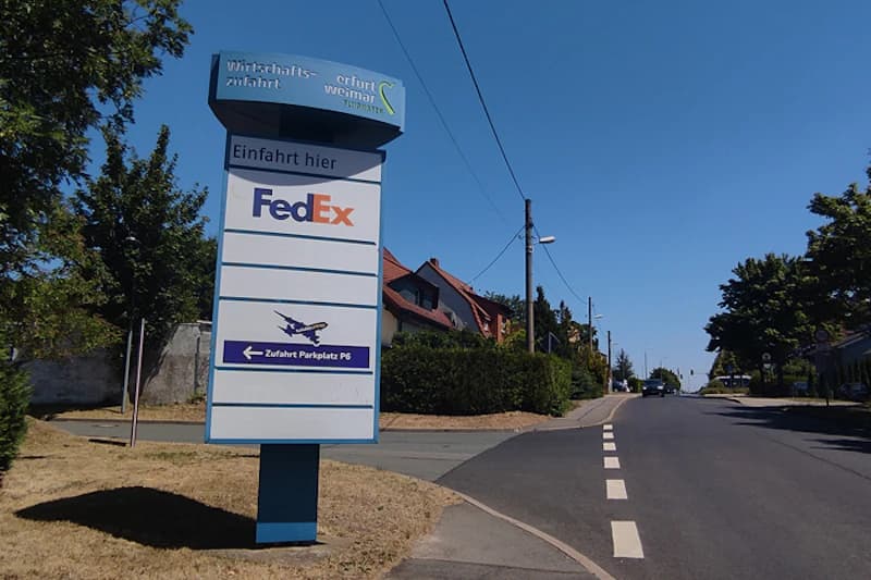 Wegweiser mit FedEx-Logo und Pfeil zu Parkplatz P6 an ruhiger Straße neben Einfamilienhäusern.