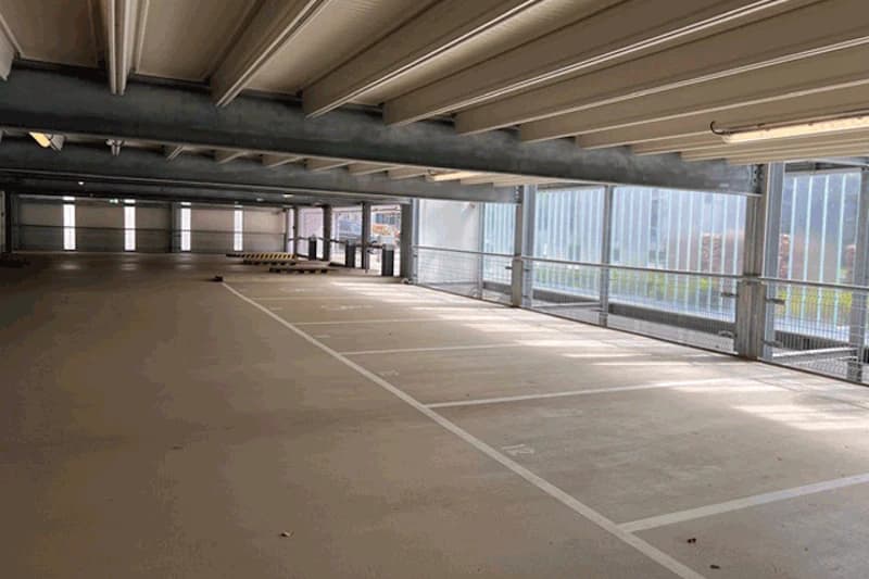 Leere Ebene eines mehrgeschossigen Parkhauses mit markierten Stellplaetzen, Betondecke und seitlichen Metallabschirmungen.