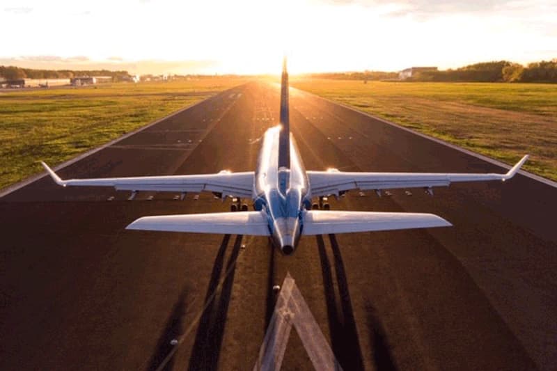 Passagierflugzeug von hinten auf Start- und Landebahn bei Sonnenuntergang, Grasflächen links und rechts.