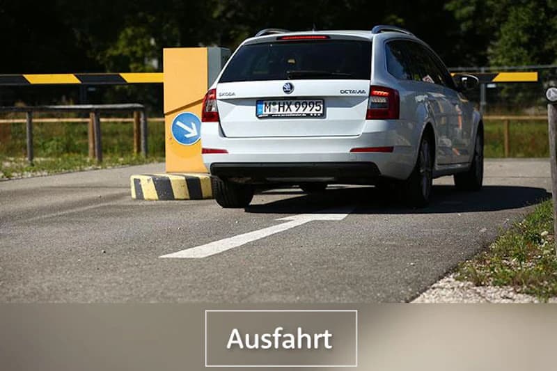 Weißer Kombi fährt durch Schranke an der Ausfahrt eines Parkplatzes, blaues Pfeilschild an der Säule sichtbar.
