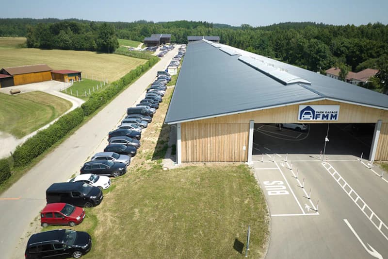 Luftbild von Außenstellplätzen entlang einer Parkhalle mit Holzgiebel und Schild FMM.