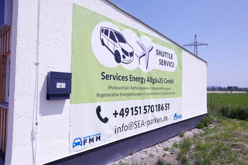 Großes Banner Shuttle Service von Services Energy Allgäu an einer weißen Hauswand mit Telefonnummer.