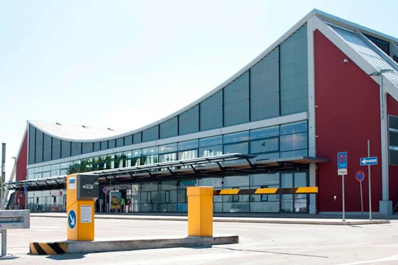 Terminalgebäude mit geschwungenem Dach und roter Fassade, davor gelbe Schranke und Kassenautomat.