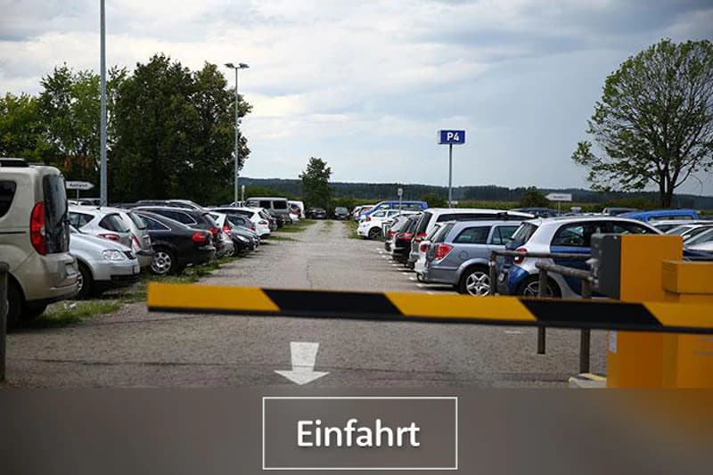 Blick über abgesenkte Schranke auf Parkplatz P4 mit Reihen geparkter Autos und Einfahrt-Hinweis.