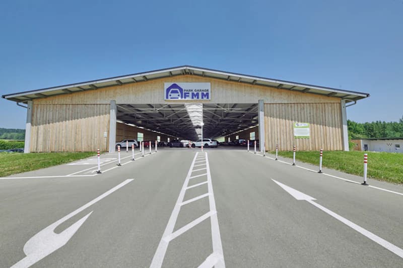 Lange Parkhalle mit Holzfassade und Schild Park Garage FMM, davor eine Zufahrt mit weißen Richtungspfeilen.