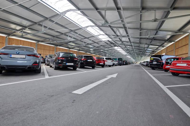 Fahrgasse in einer Parkhalle mit geparkten Autos links und rechts und weißem Richtungspfeil.