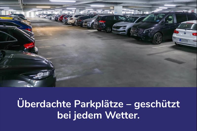 Überdachte, gut beleuchtete Parkebene mit zwei Reihen geparkter Autos in einem Parkhaus.