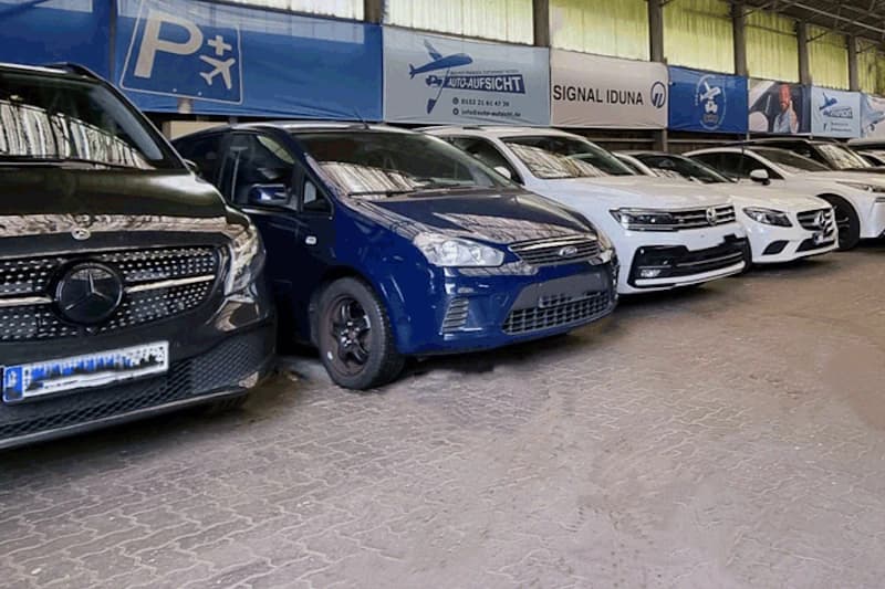 Überdachte Parkhalle mit geparkten Autos in Reihe, blaues Fahrzeug vorn, Mercedes und weiße Wagen, Banner P+ Auto-Aufsicht.