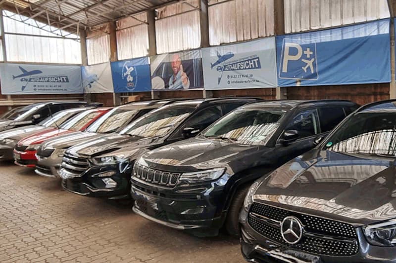 Reihe geparkter Autos in einer überdachten Halle vor Auto-Aufsicht-Bannern.