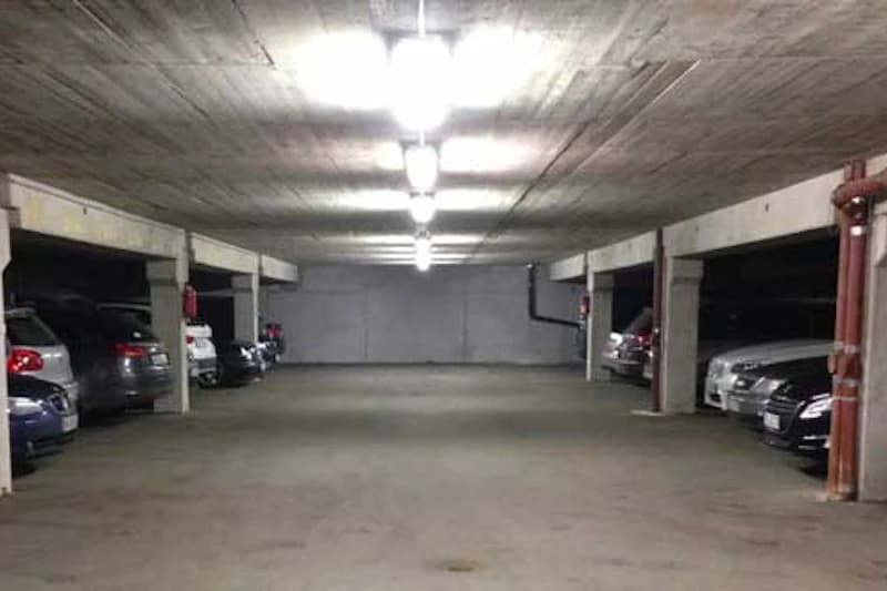 Unterirdische Parkebene mit Betonstützen, Deckenlampen und geparkten Autos an beiden Seiten.