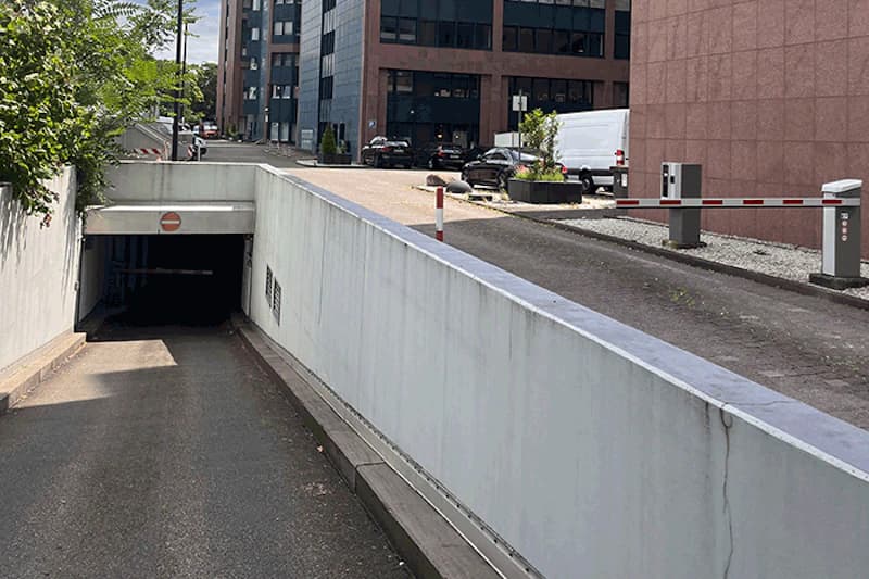 Abfahrt zur Tiefgarageneinfahrt mit abschüssiger Rampe, dunklem Tunneleingang und Schranke daneben.