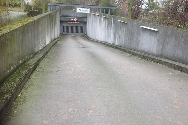 Abwärts führende Zufahrt zur Tiefgarageneinfahrt mit Schild Einfahrt und geschlossener Torklappe.
