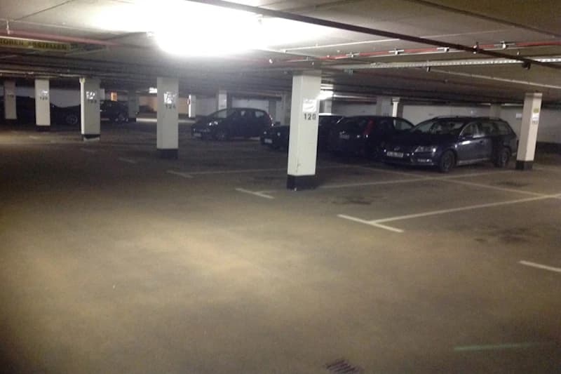Unterirdische Tiefgarage mit Pfeilern, markierten Parkplätzen und mehreren geparkten Fahrzeugen.