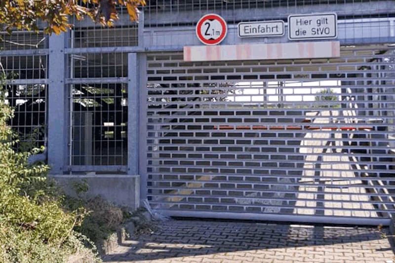 Gittertor eines Parkhauses mit Höhenbegrenzung 2,1 m, Schildern Einfahrt und Hier gilt die StVO, Rampe im Inneren sichtbar.