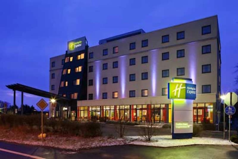 Mehrstöckiges Holiday Inn Express Hotel mit beleuchteter Fassade, Eingangsvordach und Leuchtschild bei Dämmerung.