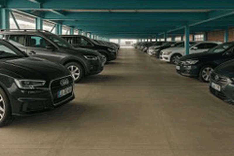 Mehrgeschossiges Parkdeck mit Reihen geparkter Autos, türkisfarbenen Stützen und zentraler Fahrspur.