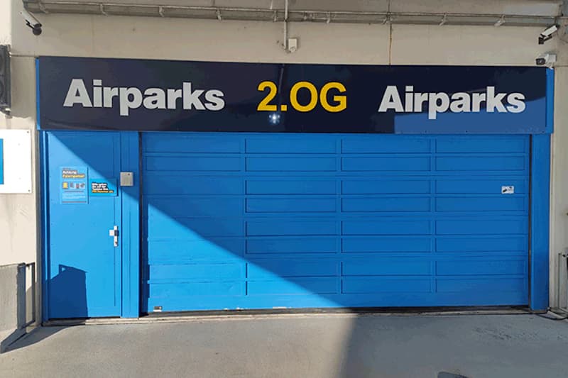 Blaues Rolltor mit Schriftzug Airparks 2.0G, links kleine Seitentür und Überwachungskamera.