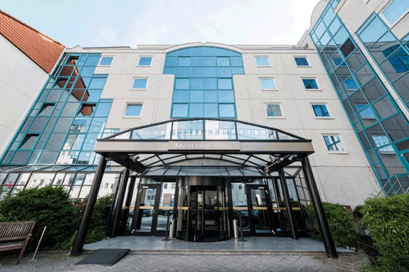 Fassade des Mercure Hotels mit Glasvordach, drehbarer Eingangstür und mehrstöckigen Glasfenstern.