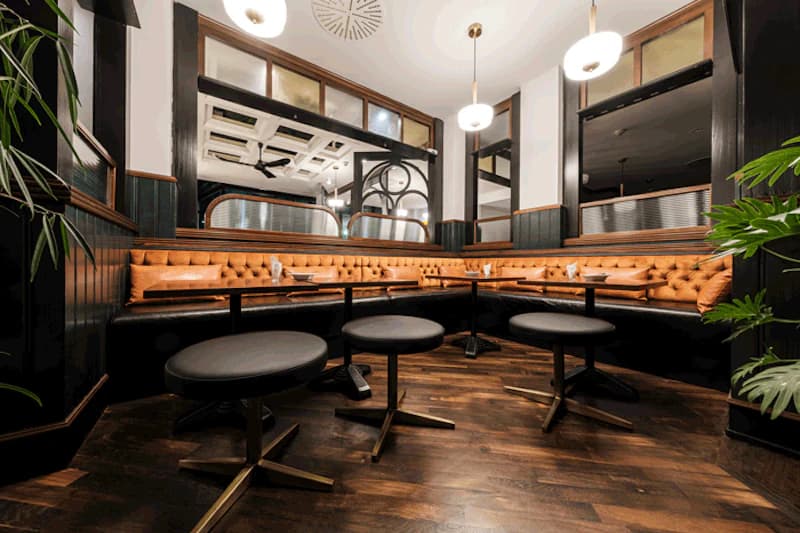 Gemütliche Hotelbar mit brauner gesteppter Ledersitzbank, runden Hockern und dunklem Holzboden.