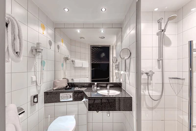 Kompaktes weiß gekacheltes Badezimmer mit schwarzer Waschbeckenplatte, Spiegel, Dusche und Toilette.