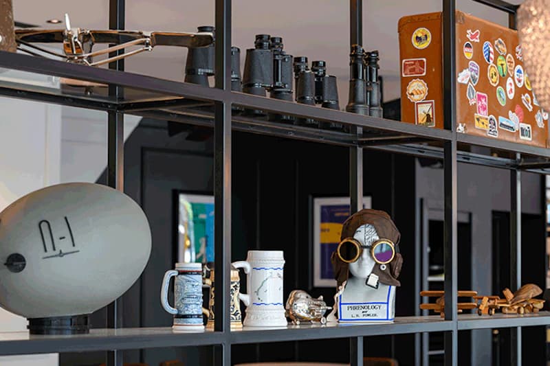 Offenes Regal mit Modellpropeller, Zeppelinskulptur, Ferngläsern, Bierkrügen, Reisekoffer und Fliegerkopf mit Schutzbrille.