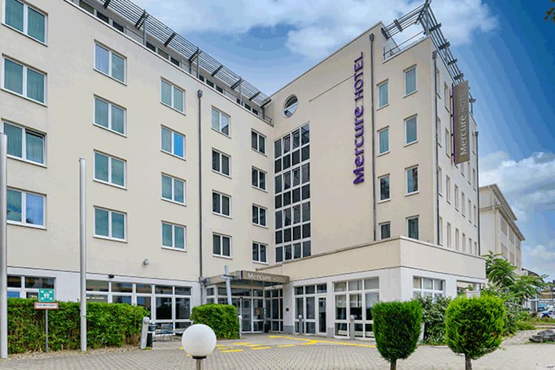 Eingangsbereich des Mercure Hotel Frankfurt Neu-Isenburg mit mehrstöckigem beiger Fassade und gepflasterter Vorfahrt.