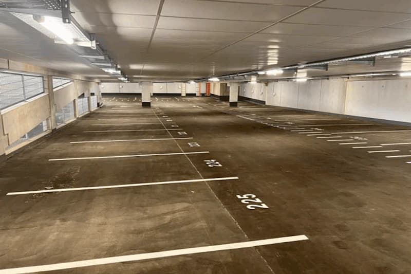 Leeres beleuchtetes Parkdeck in Tiefgarage mit markierten nummerierten Stellplätzen und Betonpfeilern.
