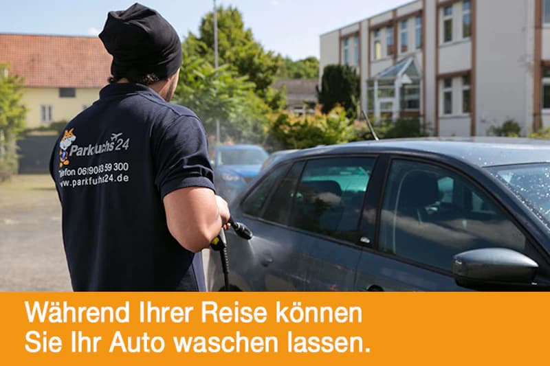 Mann mit Parkfuchs24-Shirt spritzt mit Hochdruckreiniger ein geparktes Auto in einem Außenbereich.
