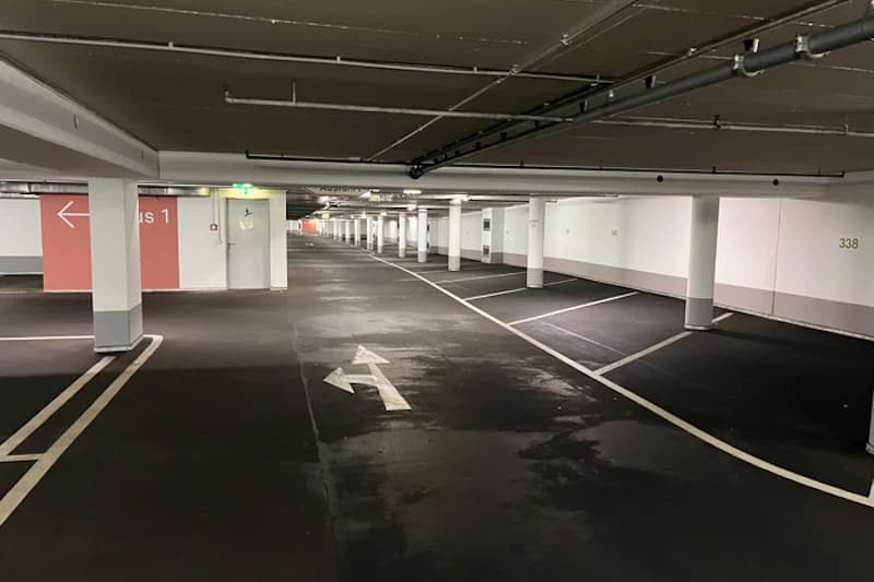 Leere Tiefgarage mit Fahrtrichtungspfeil, markierten Stellplätzen und Reihen von Stützpfeilern.