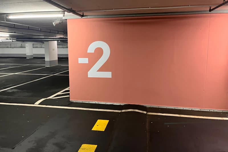 Tiefgarage Ebene -2: große weiße Zahl auf rosa Wand, leere Parkbuchten, Pfeiler und gelbe Bodenmarkierungen.