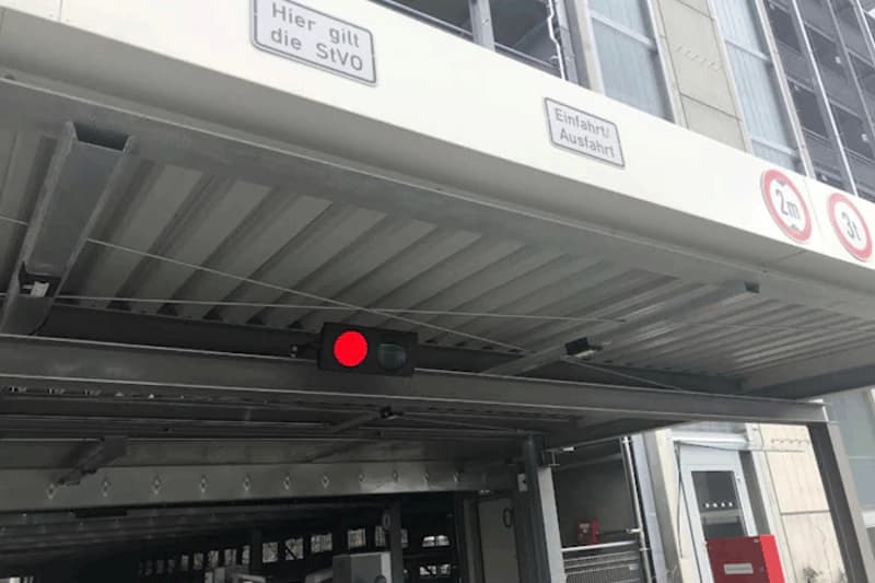 Einfahrt eines Parkhauses mit roter Ampel, sichtbarer Decke und mehreren Verkehrs- und Hinweisschildern.