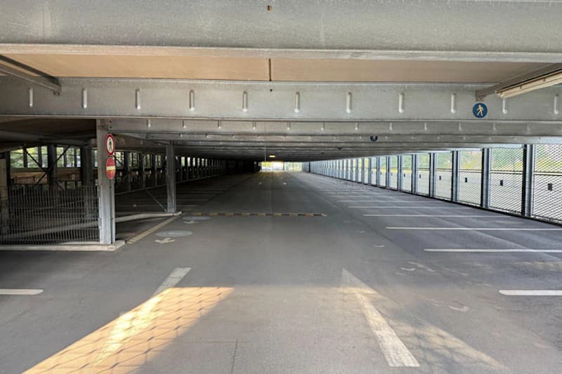 Leeres Parkdeck eines mehrgeschossigen Parkhauses mit Fahrspur, Parkplätzen rechts und Metallgeländern.