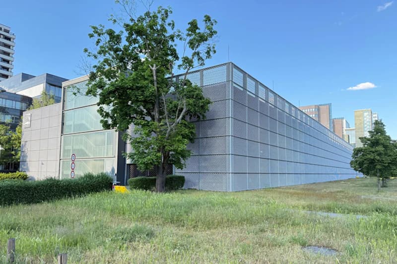 Mehrstöckiges Parkhaus mit perforierter Metallfassade, Wiese und Bäume im Vordergrund.